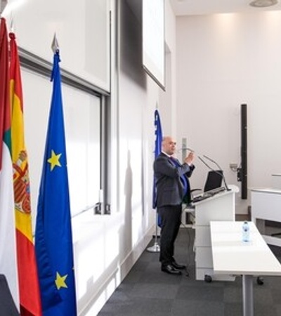 A speaker presenting in a modern classroom setting with flags in the background.