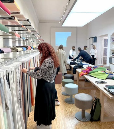 A woman browsing through fabric swatches in a modern textile store with other customers and staff in the background.