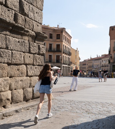 A young woman walks through an archway in a historic city square on a sunny day.