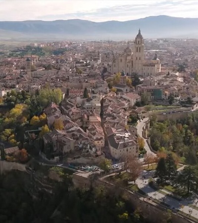 Aerial view of a historic European city with a large cathedral dominating the skyline, surrounded by autumn-colored trees and old buildings.