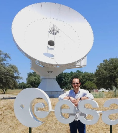 A person stands in front of a large satellite dish with the ESA logo.