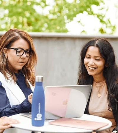 Three professionals are discussing over a laptop at an outdoor table.