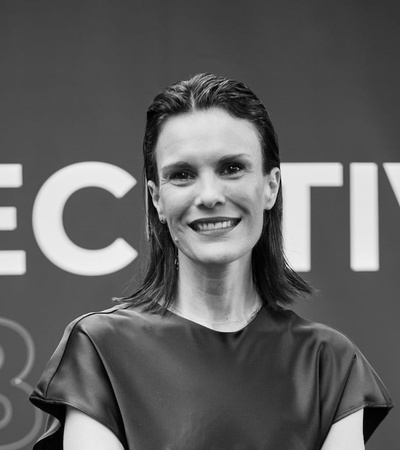 Black and white photo of a smiling woman standing in front of a background with the word 'EXECUTIVE'.