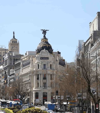 A bustling urban scene showcasing a grand building with a statue on top, and a busy street filled with cars.