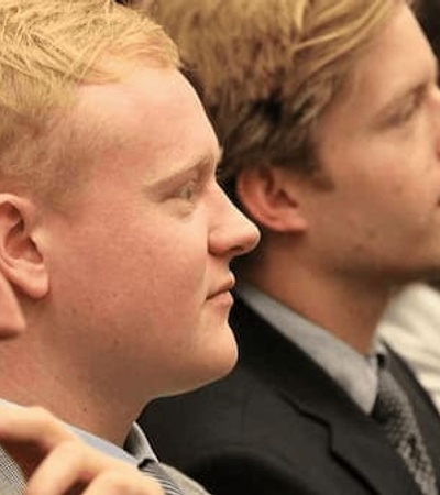 A row of young adults, primarily men, seated and focusing on something in front of them.