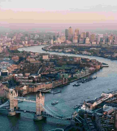 Aerial view of London showing the River Thames and iconic landmarks such as Tower Bridge during sunset.