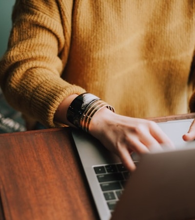 A person is typing on a laptop while wearing a cozy sweater and bracelets.