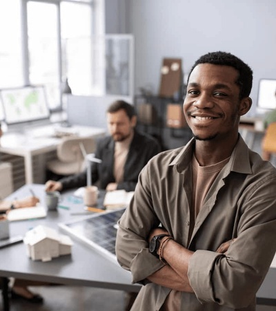 A young man smiling confidently in a busy office environment, with colleagues working in the background.