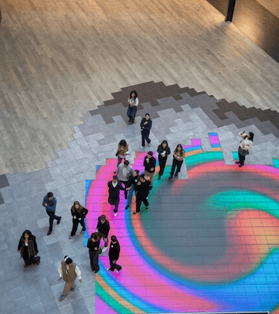 A group of people standing on a colorful illuminated floor in a spacious indoor area.