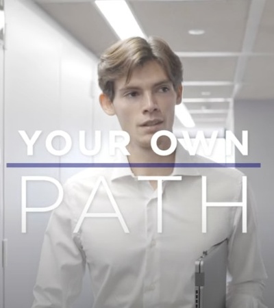 A young man in an office corridor, with the text 'YOUR OWN PATH' overlaying the image.