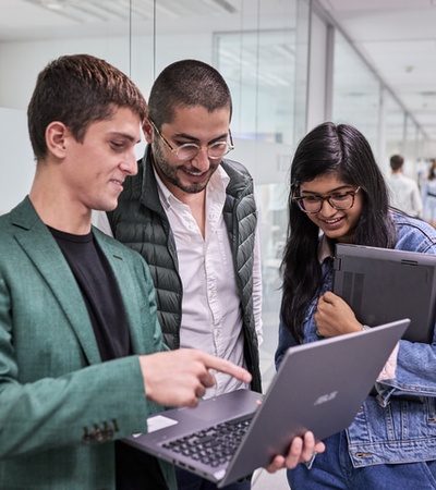 A group of three people collaborating over a laptop in an office setting.