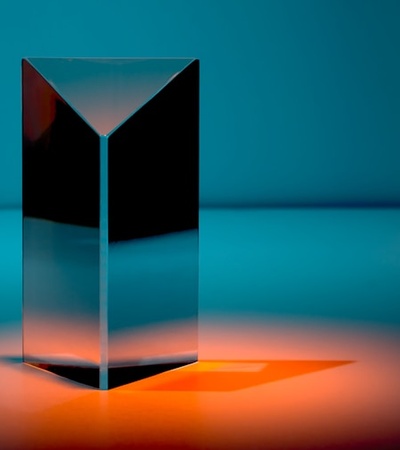 A reflective geometric object casting a soft orange glow on a blue background.