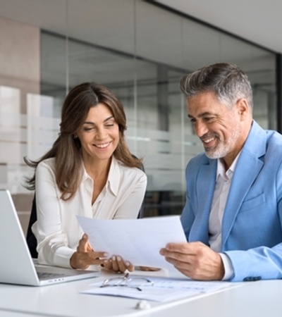 A woman and a man are smiling and discussing a document in a modern office setting.