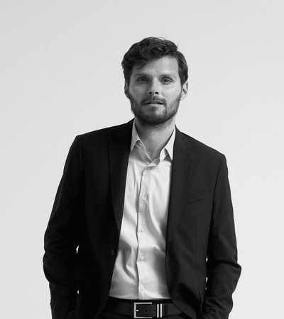 A black and white photo of a young man in a suit standing with his hands in his pockets.