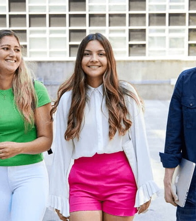 Three young adults walking and chatting cheerfully in an urban setting.