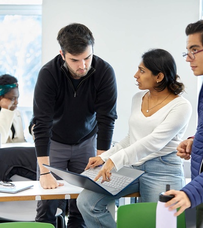 A group of students collaborating around a laptop in a classroom setting.
