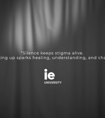 An inspirational quote on a gray curtain background, stating the impact of speaking up against silence, attributed to IE University.