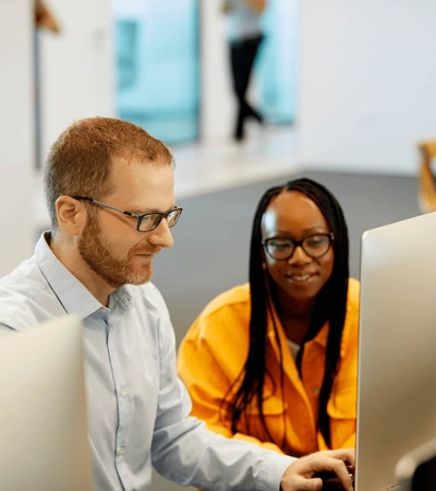 A man and a woman working together on computers in a modern office setting.