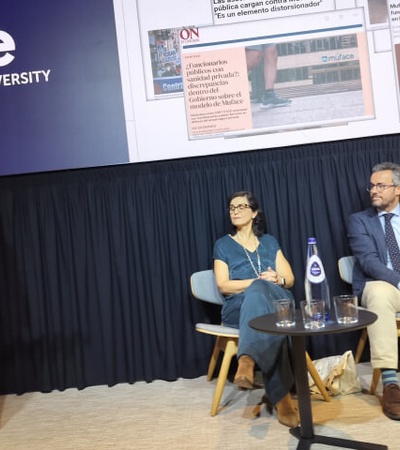 A woman is speaking at a podium during a panel discussion at IE University with three panelists seated in the background.