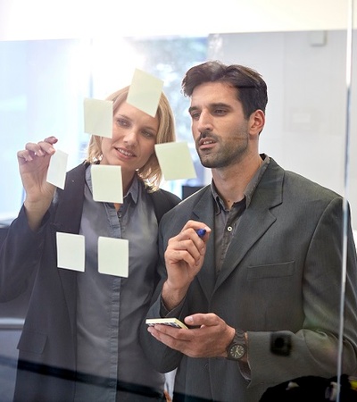 Men and woman sticking post-it in a transparent white  board