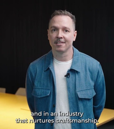 A man in a denim jacket speaks in an office environment with a subtitle text displayed.