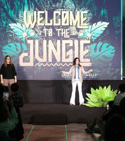 Two people standing on stage with a 'Welcome to the Jungle' backdrop at a corporate event, as the audience watches.