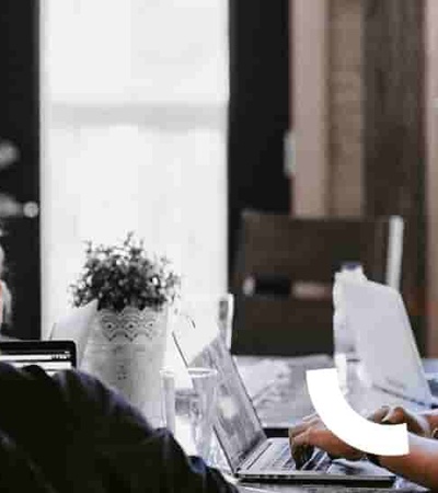 A group of people working together in a modern office environment with laptops and headphones.