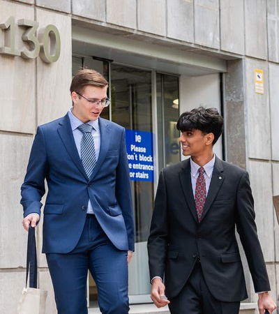 Two young men in business attire are walking together outside a building.