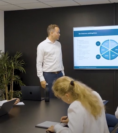 A business meeting in a conference room with participants discussing a presentation on a screen.