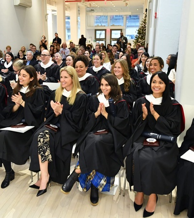 A group of people in graduation robes clapping in a crowded room.