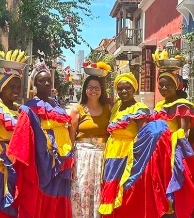 A group of women dressed in colorful traditional attire poses together in a vibrant street.