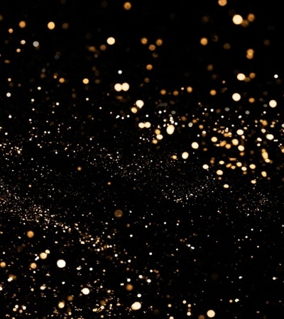 Abstract image of golden sparkles scattered across a dark background.