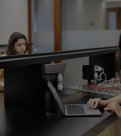 A young woman is using a laptop in a modern classroom setting while another student works in the background.