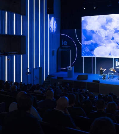 An auditorium filled with an audience watching a presentation on a large screen.