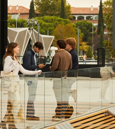 A group of people conversing on a modern outdoor plaza with transparent barriers and urban buildings in the background.