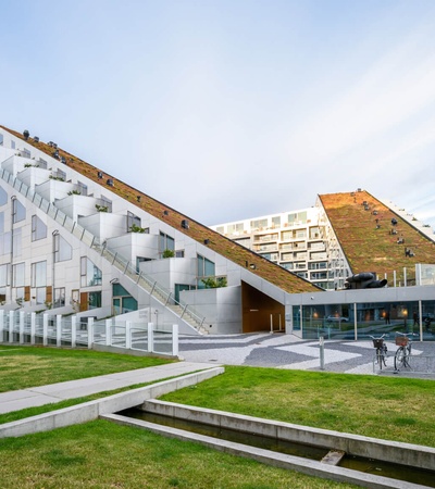 Modern architectural building featuring an angular design and a predominantly white facade, surrounded by a green lawn and a pedestrian walkway.