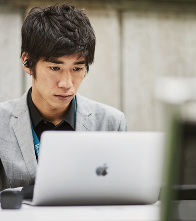 A young man in a suit sits at a table working on a laptop.
