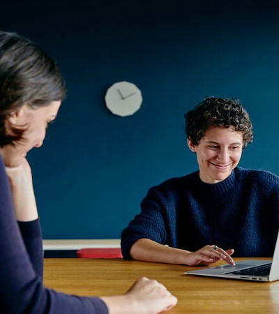 Two women are engaged in a collaborative discussion while working on a laptop.