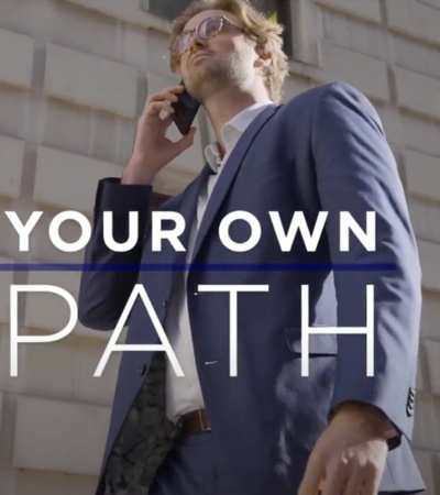 A man in a suit is walking and talking on a cellphone in front of a building, with the phrase 'YOUR OWN PATH' overlaid on the image.