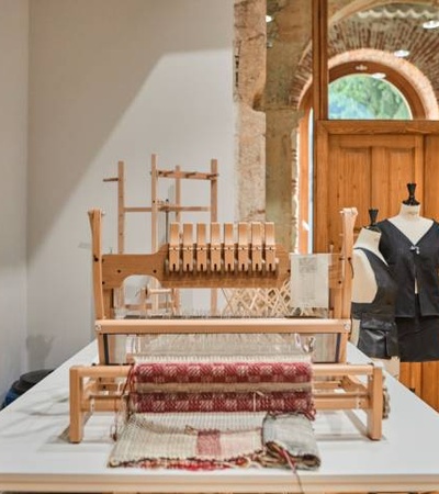 A traditional weaving loom and a tailor's mannequin displayed inside a room with rustic architectural elements.