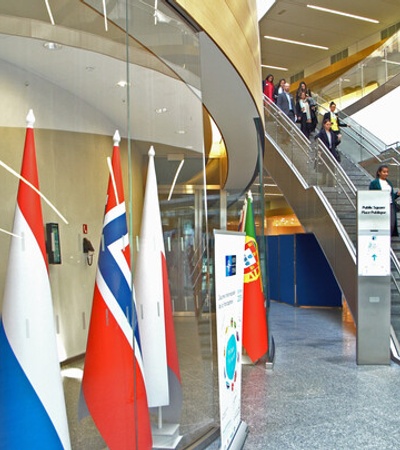 An interior view of a modern building featuring flags and people walking up the stairs.