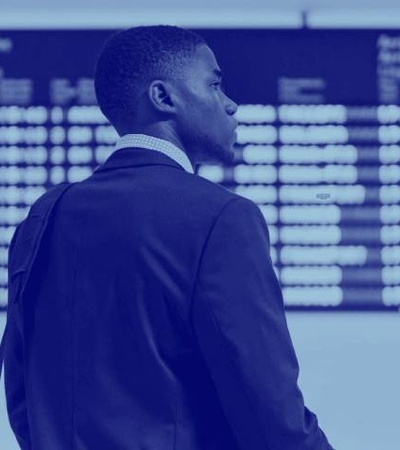 A businessman in a suit standing at an airport looking at the flight information monitor.