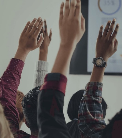 A group of people raising their hands in a classroom setting during a presentation.