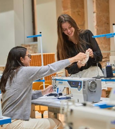 Two women are engaged in a sewing activity at a well-equipped workspace.