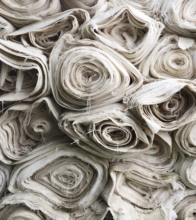 The image shows a stack of rolled fabric in neutral tones.