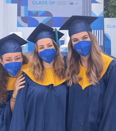 Three graduates wearing blue caps, gowns, and masks pose for a photo at their graduation ceremony.