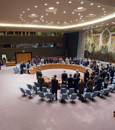 A formal meeting in the United Nations Security Council chamber with delegates standing in a circle.
