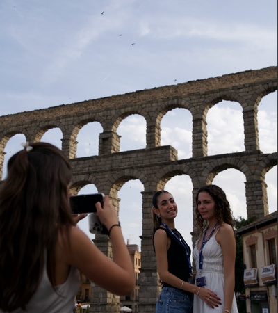 Three young women are posing for a photo in front of an ancient aqueduct in a lively setting.