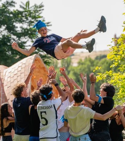 A young man performs a flip being tossed by a group of friends in a park