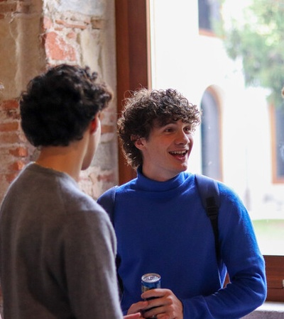 A group of four young men are having a lively conversation indoors near a window.